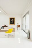 Gelber Drehsessel und helles Designersofa, im Hintergrund antike Kleinmöbel und Gemälde im Goldrahmen an Wand, in minimalistischer Loftwohnung