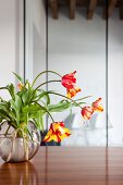 Tulpenstrauss mit rotgelben Blüten in Kugelvase auf Edelholztisch
