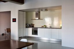 View from dining area into open-plan, white kitchen with illuminated niche