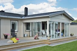 Pale grey wooden bungalow with glazed veranda and lawn in foreground