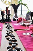 Festlich gedeckter Tisch mit pinkfarbenem Tischset und schwarzen, glänzenden Steinen