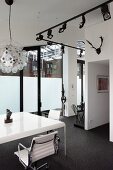 Weisser Tisch mit eleganten Bürostühlen und schwarzes Licht-Schienensystem mit Strahlern in Loftwohnung
