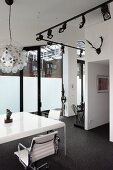 White table with elegant office chairs and lighting system with spotlights on black rails in loft apartment