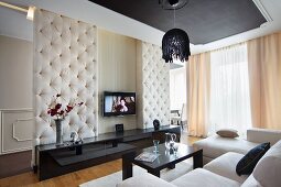 Elegant interior with suspended ceiling, white sofa combination and black sideboard against button-tufted partition wall