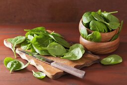 An arrangement of spinach leaves in a wooden bowl and on a chopping board