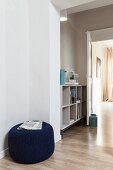 Newspaper on dark blue pouffe and open-fronted shelves in hallway