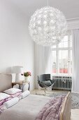 Elegant bedroom with upholstered bedstead, grey designer chair and large, white, spherical lampshade