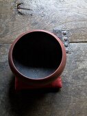Rusty red ceramic bowl with black inside on rustic wooden surface
