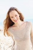 A happy young woman on a beach wearing a crocheted jumper