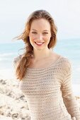 A happy young woman on a beach wearing a crocheted jumper