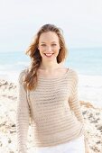 A happy young woman on a beach wearing a crocheted jumper