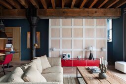 Seating area with sofa and rustic table in converted industrial building; low, red sideboard against panelled partition leading to bedroom