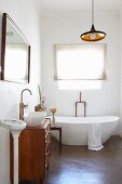 Bad mit puristischen Installationsarmaturen und Designerwanne, Waschtischkommode, Spiegel, Personenwaage und Leuchte im Retrostil