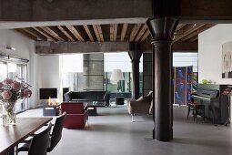 Loft apartment with black metal pillar under girder structure, dining area to one side and lounge area with leather retro armchairs