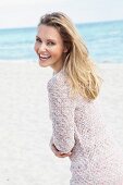 A blonde woman on a beach wearing a long, knitted jumper