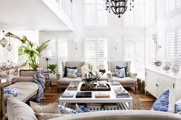 Ecru sofa set around white coffee table in double-height interior with closed window shutters