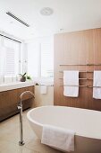 Badezimmer mit heller Holzverkleidung, Steinfliesenboden und moderner freistehender Badwanne