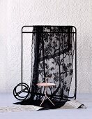 Side table and black voile cloth hanging over clothes rail against white structured wallpaper