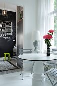 Round table with chunky, carved, white pedestal next to window with doorway to kitchen in background