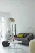 Dekokissen auf grauem Retro Sofa vor geweisselter Ziegelwand in Wohnraum mit traditionellem Flair