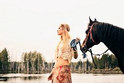 Junge blonde Frau im Hippie-Stil mit Pferd an See