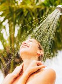 A young woman under an outdoor shower with palm trees in the background