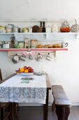 Lace tablecloth on dining table, antique bench and retro crockery on wall-mounted shelves
