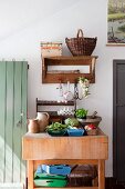 Fresh vegetables and kitchen utensils on rustic wooden kitchen table below wooden shelf on wall