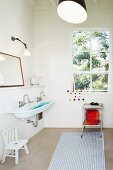Simple bathroom with white and blue striped rug, trolley below window and trough-style sink to one side