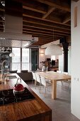 Kitchen counter with rustic wooden worksurface and extractor hood; modern dining area below paper pendant lamp