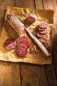 Salami, sliced, on a piece of paper with a knife