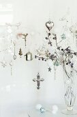 Glass vase of shiny silver Christmas decorations hanging from white-painted twigs