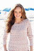A young, long-haired woman on a beach wearing a knitted jumper