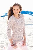 A young, long-haired woman on a beach wearing a knitted jumper