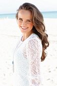 A young, long-haired woman on a beach wearing a white lace dress