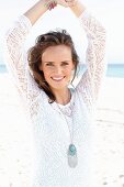 A young, long-haired woman on a beach wearing a white lace dress