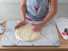 Dough being patted flat on a marble slab