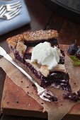 A slice of mulberry pie with cream with a bite taken out