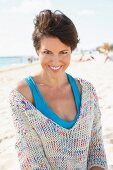 A woman with short, brown hair on the beach wearing a light knitted jumper