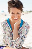 A woman with short, brown hair on a beach wearing a light knitted jumper