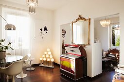 Retro jukebox under gilt-framed, antique mirror, modern artwork and unusual light sculpture in white interior