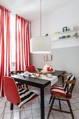 A dining area with old and new chairs against a window with red-and-white stripped curtains in a renovated kitchen