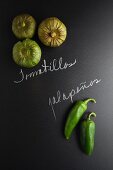 Tomatillos and jalapeños on a slate surface with labels