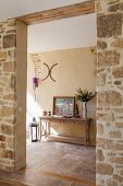A wide entrance through a natural stone wall with a view of a wall table in a traditional hallway