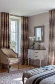 Antique armchair next to window with floor-length curtains and white console table in corner of bedroom