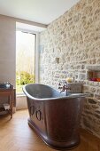 Vintage metal bathtub against stone wall in renovated bathroom with window