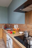 Kitchen counter with pale wooden worksurface and cupboards against wall painted pale blue