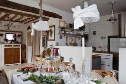 Festively set table below decorated, wire mesh pendant lamps in open-plan country-house interior