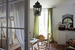 Table and wooden chairs next to window with green, floor-length curtains in rustic interior