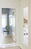 View into bedroom and bathroom with pale blue, panelled walls and chair with black and white upholstery